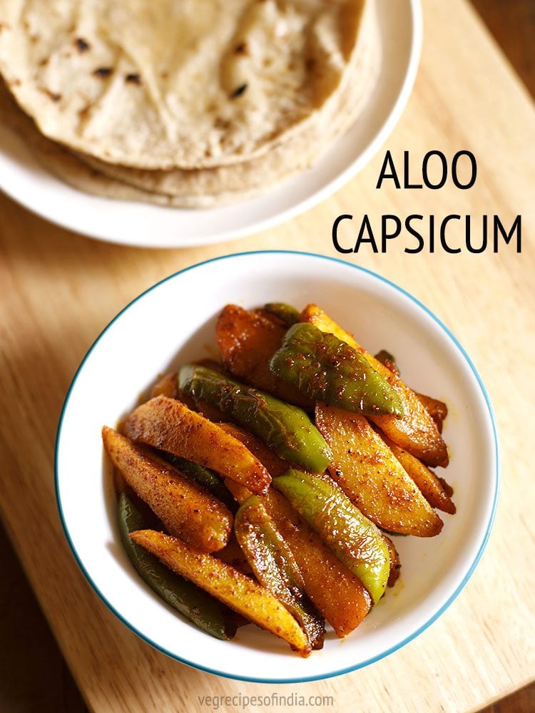 top shot of aloo capsicum or aloo shimla mirch ki sabji in a white green rimmed bowl on a beige colored wooden board