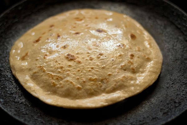 the second side of the aloo paratha has been brushed with oil and the whole paratha is puffed up in the center like a ufo.