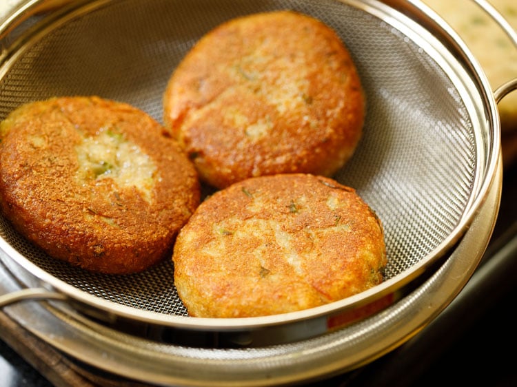 fried aloo tikki placed in a strainer kept on top of a bowl. 