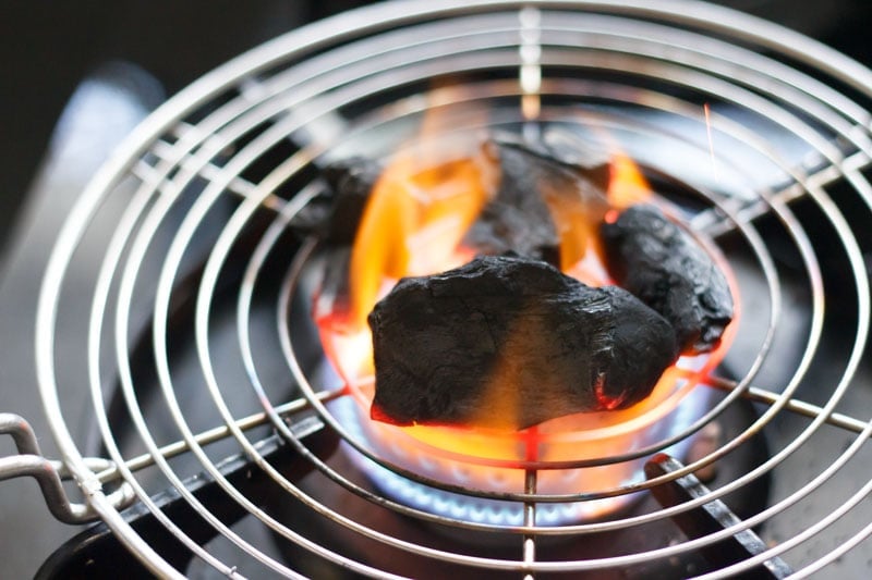 coal pieces on a round wired tray on stove-top burner
