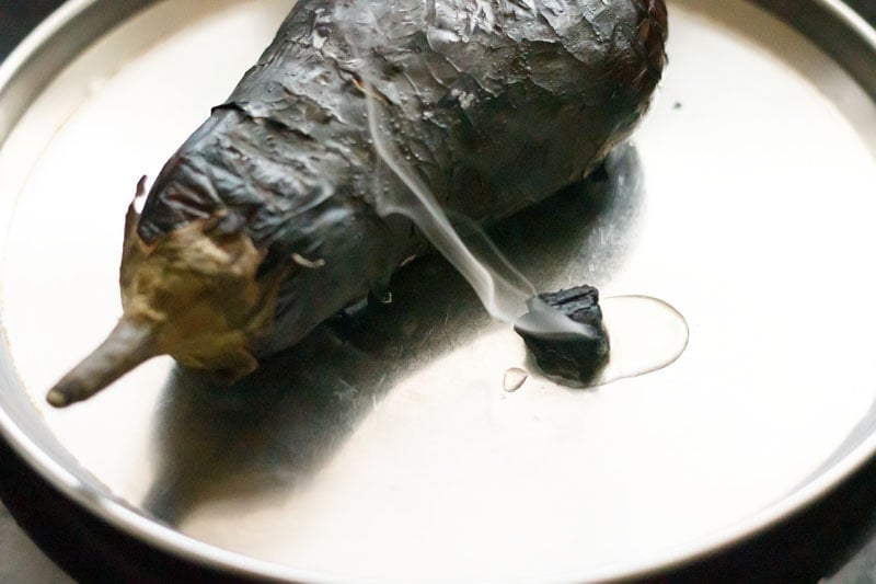 smoked charcoal with oil dripping on it and sides placed close to the roasted eggplant in a steel plate