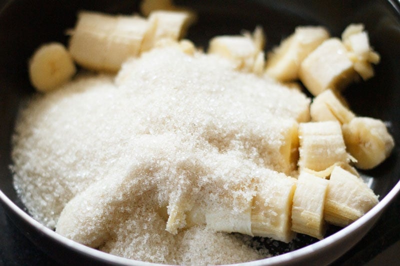 Top shot of sliced bananas with sugar on top in black bowl