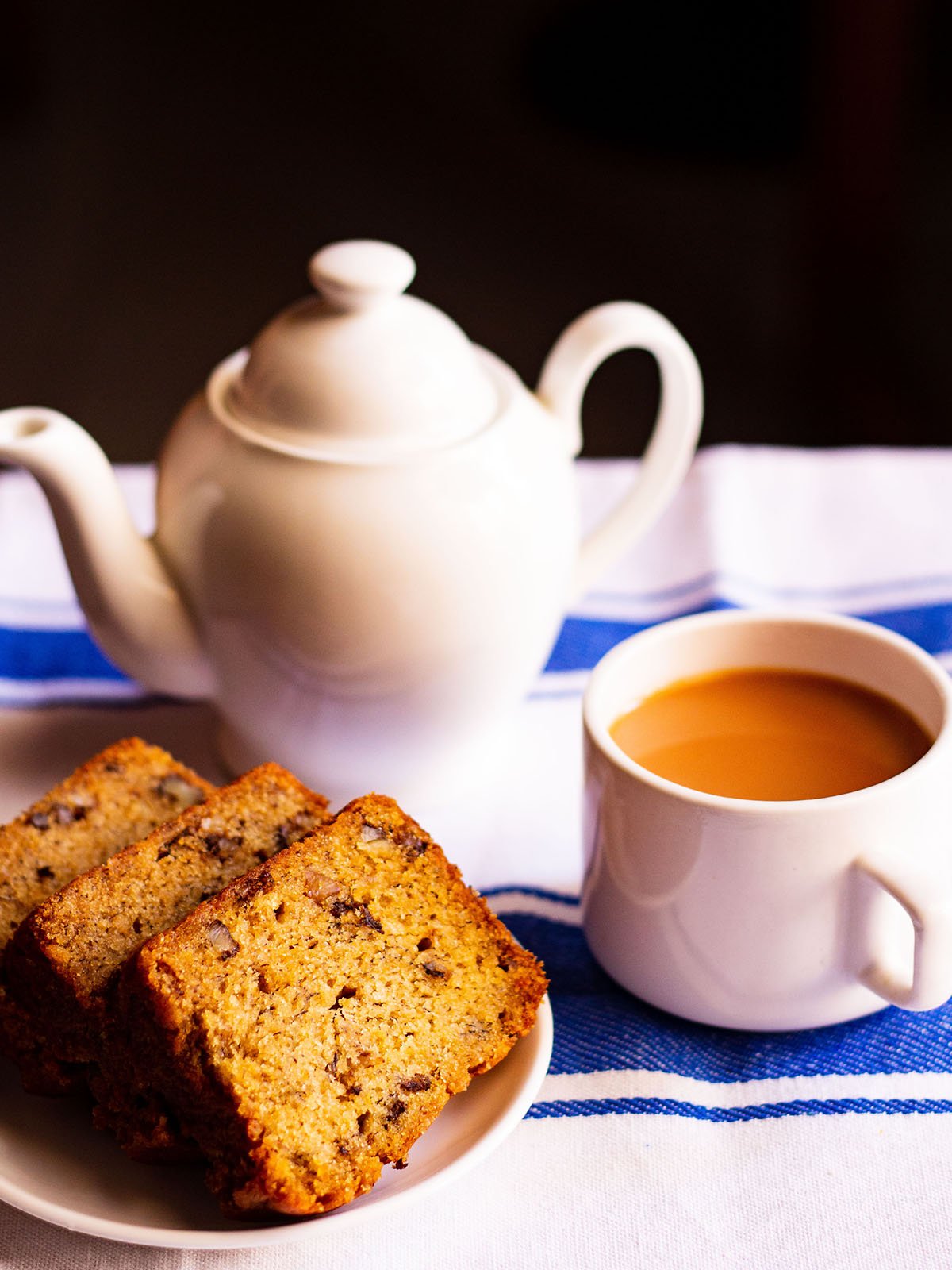 sliced eggless banana cake slices on a white plate with a white cup of tea and white tea pot
