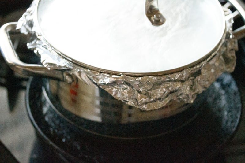 Top shot of closed pot with aluminum foil placed on a black tawa (skillet)