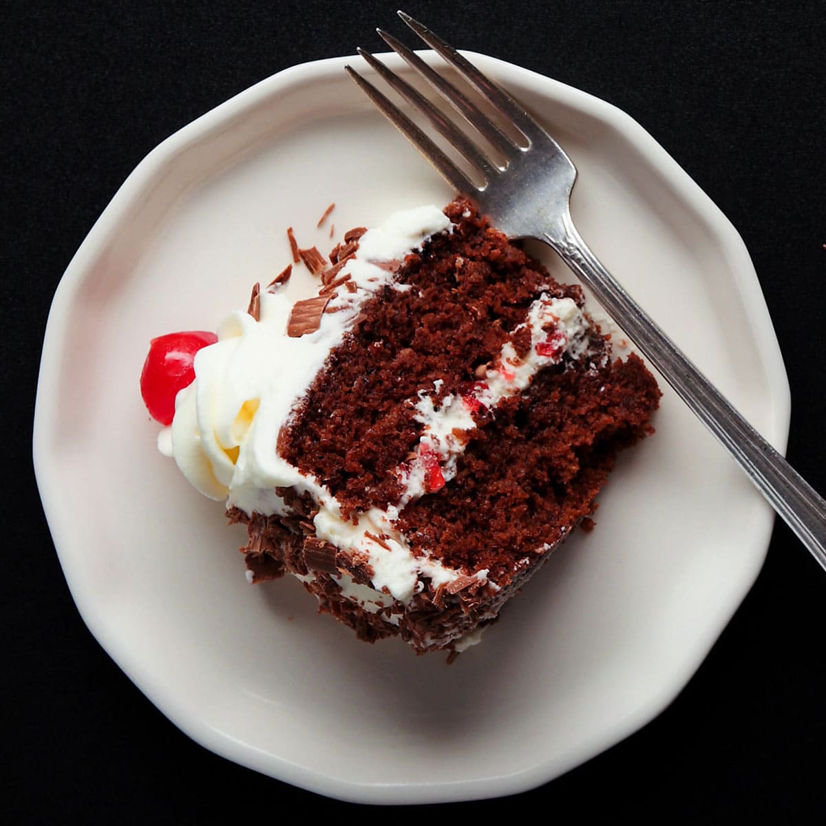 overhead shot of a slice of black forest cake on its side on a white dessert plate with a silver fork