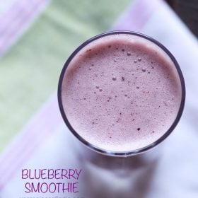 overhead shot of vegan blueberry smoothie in a glass placed on a white, pink and green cotton napkin with text layovers