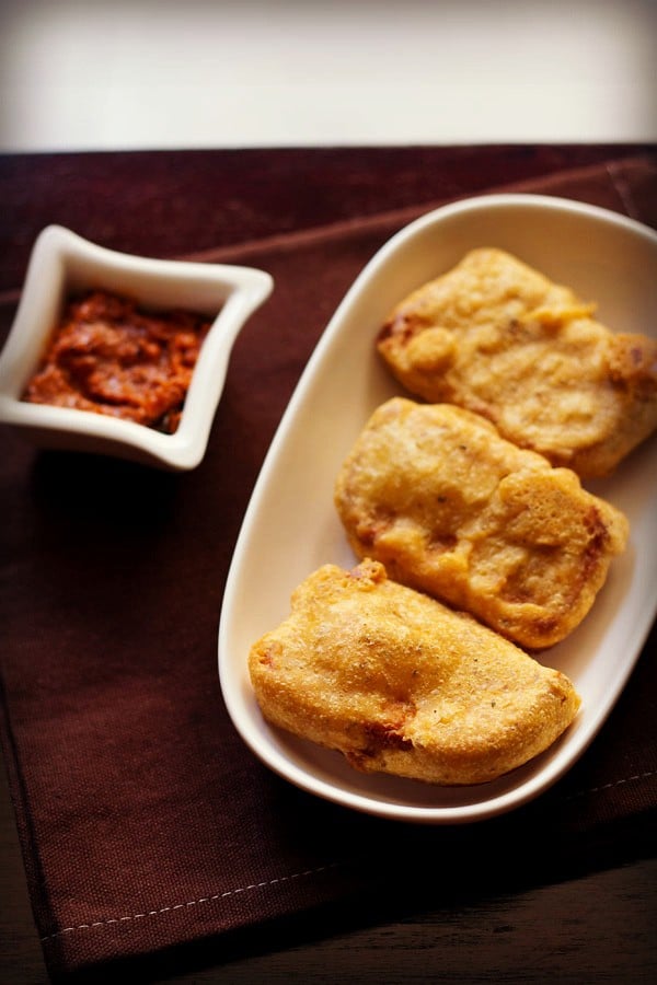 bread bajji in an oval white plate with a side of tomato chutney on a dark brown napkin