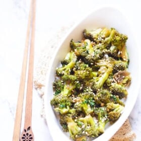 broccoli stir fry in a white oval plate with wooden chopsticks by the side