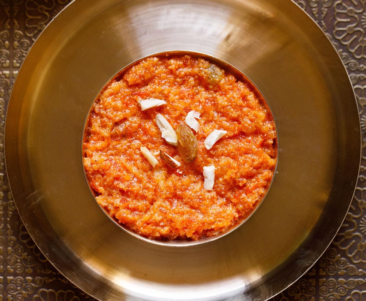 overhead shot of carrot halwa filled in a bronze bowl placed on a bronze plate