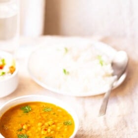 chana dal in a white bowl garnished and a white plate filled with cooked rice