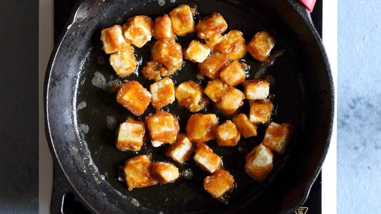 cubes of paneer are golden brown from frying in a skillet of oil