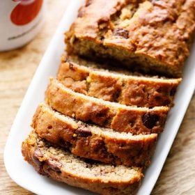 Chocolate Chip Banana Bread Loaf sliced on a white platter placed on a wooden board.