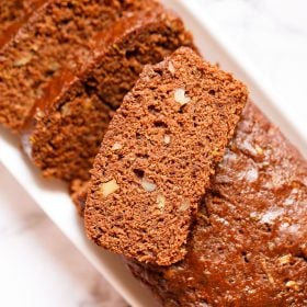 chocolate zucchini bread partly sliced with one slice kept on top of the loaf on a white rectangular tray on a white marble background