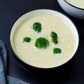 cream of broccoli soup topped with broccoli florets in a black rimmed white bowl on a black board
