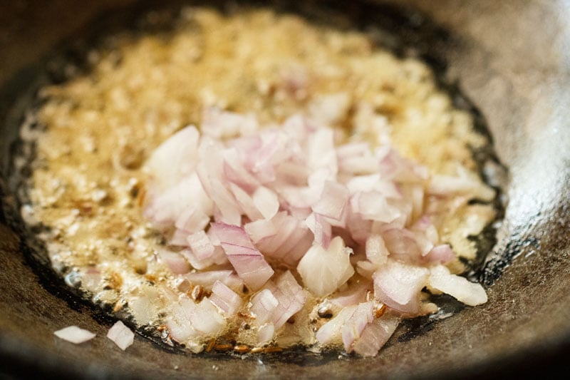 Cumin seeds, chopped onions, and oil frying in kadai