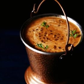 dal makhani garnished with coriander leaves and served in a fancy copper bucket with text layovers.
