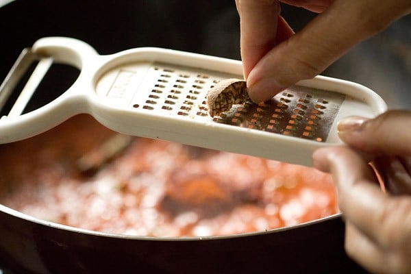 nutmeg being grated on a small grater above the pan