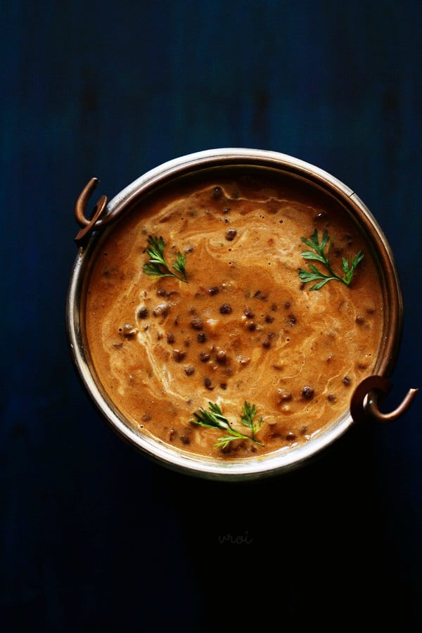 top shot of dal makhani garnished with three small coriander sprigs served in a small bucket on a dark blue board