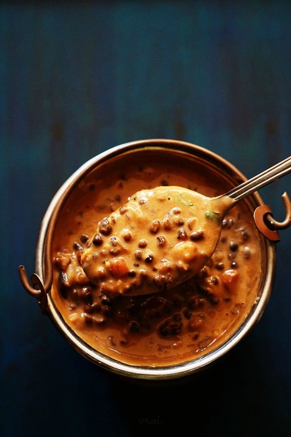 dal makhani served in a small and taken in a spoon on a dark blue board