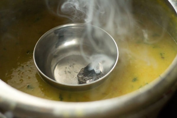 the bowl with the charcoal and the fumes emanating from it has been kept on the dal in the pressure cooker