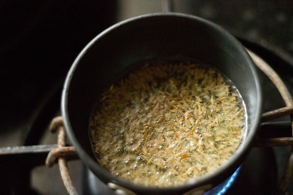 cumin seeds being fried in oil in a small round pan
