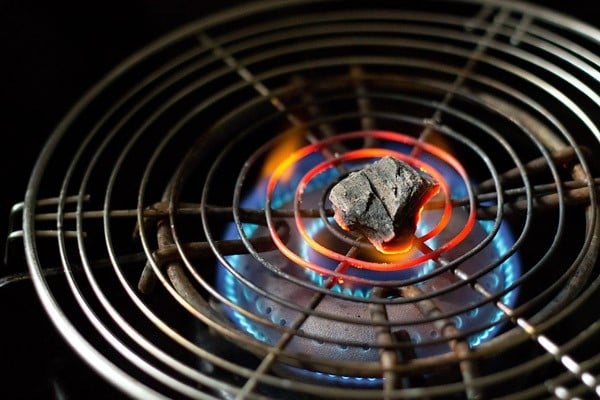 a small piece of charcoal kept on a wired pan and being burnt on a gas-stove flame