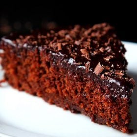 A triangular slice of eggless chocolate cake on a white plate