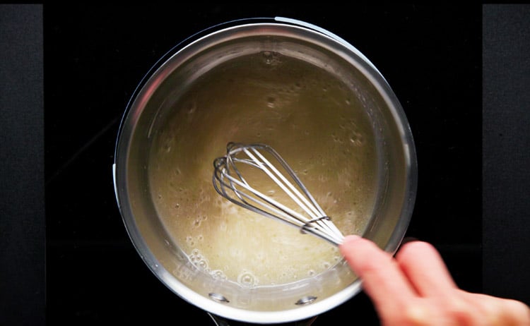 mixing the sugar in the almond milk with a whisk while the sauce pan is kept on low heat