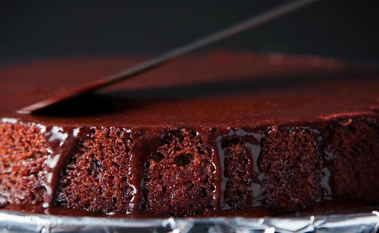 spreading the vegan icing with an offset spatula on the sides and top of the eggless chocolate cake.