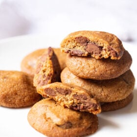 eggless chocolate chip cookies stacked with some halved cookies on a white plate
