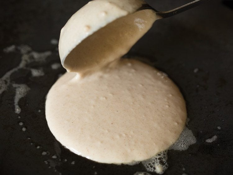 pouring whole wheat pancake batter on skillet with a ladle.