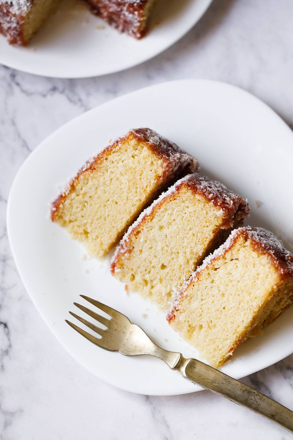 top shot of thick slices of eggless vanilla cake on a square shaped white plate woth a brass fork on the plate