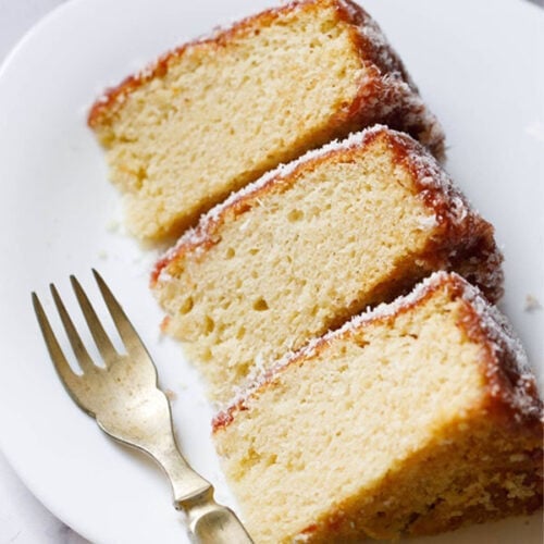 close up shot of thick slices of eggless vanilla cake on a square shaped white plate with fork by the side