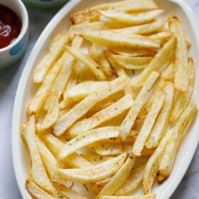 white serving tray filled with homemade french fries next to small dipping bowls of ketchup and green chutney