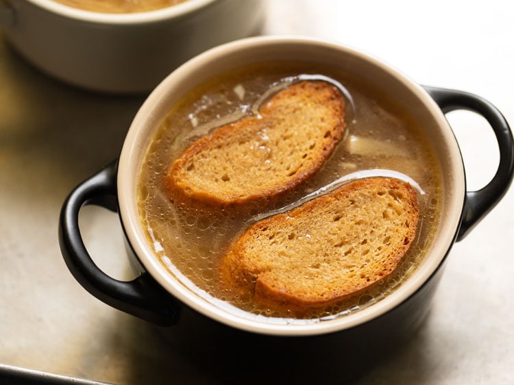 toasted baguette slices being placed on the soup.