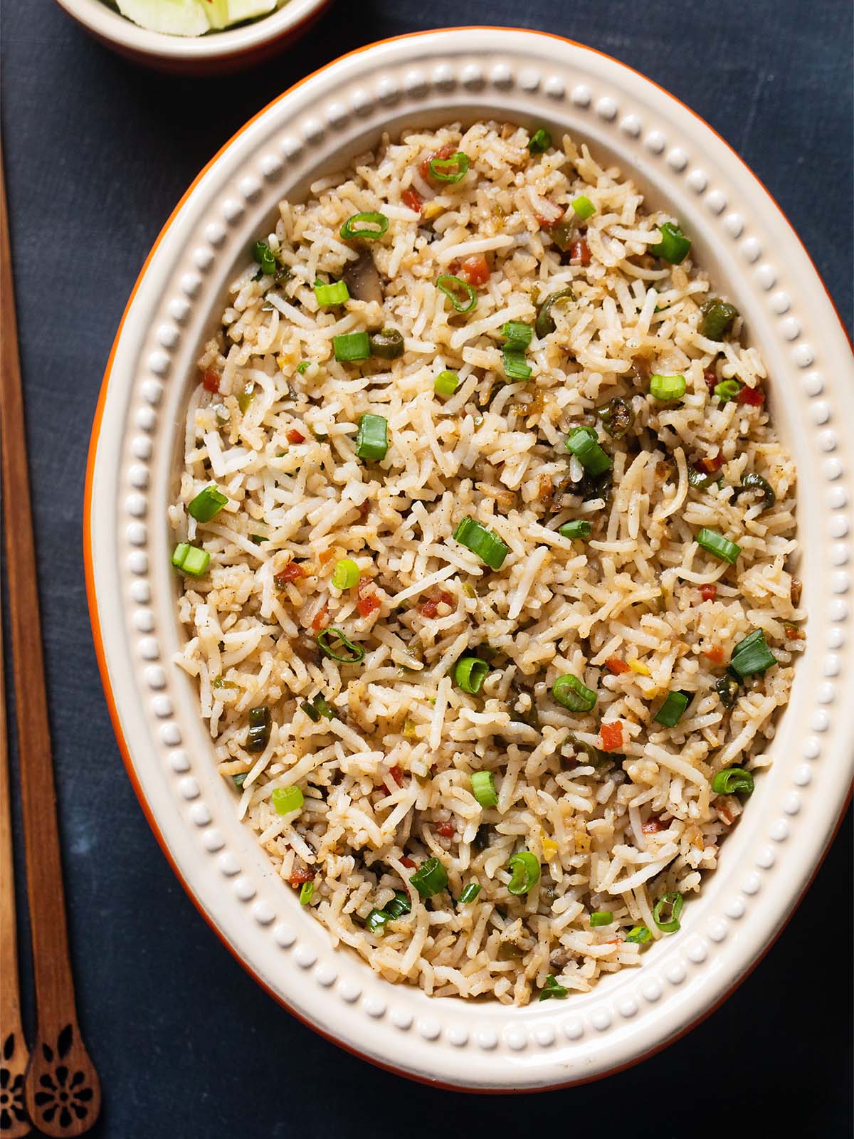 fried rice in a oval ceramic bowl with wooden chopsticks at side on a slate black board