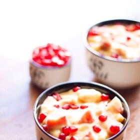 two black and white bowls filled with fruit custard and garnished with pomegranate arils