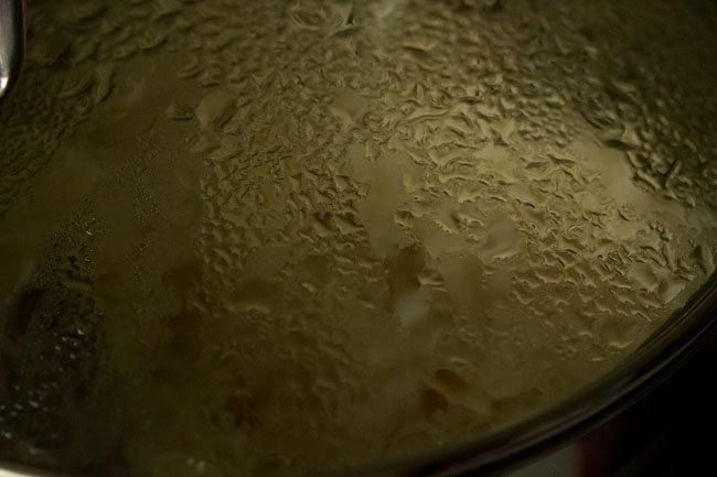 rice being simmered inside the pan covered with lid moistened with water droplets
