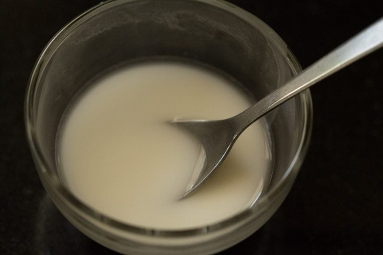 cornstarch paste being stirred with a spoon in glass bowl