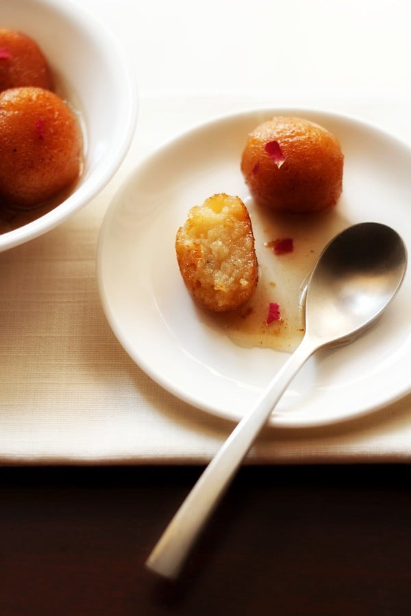gulab jamun halved with a spoon on white plate