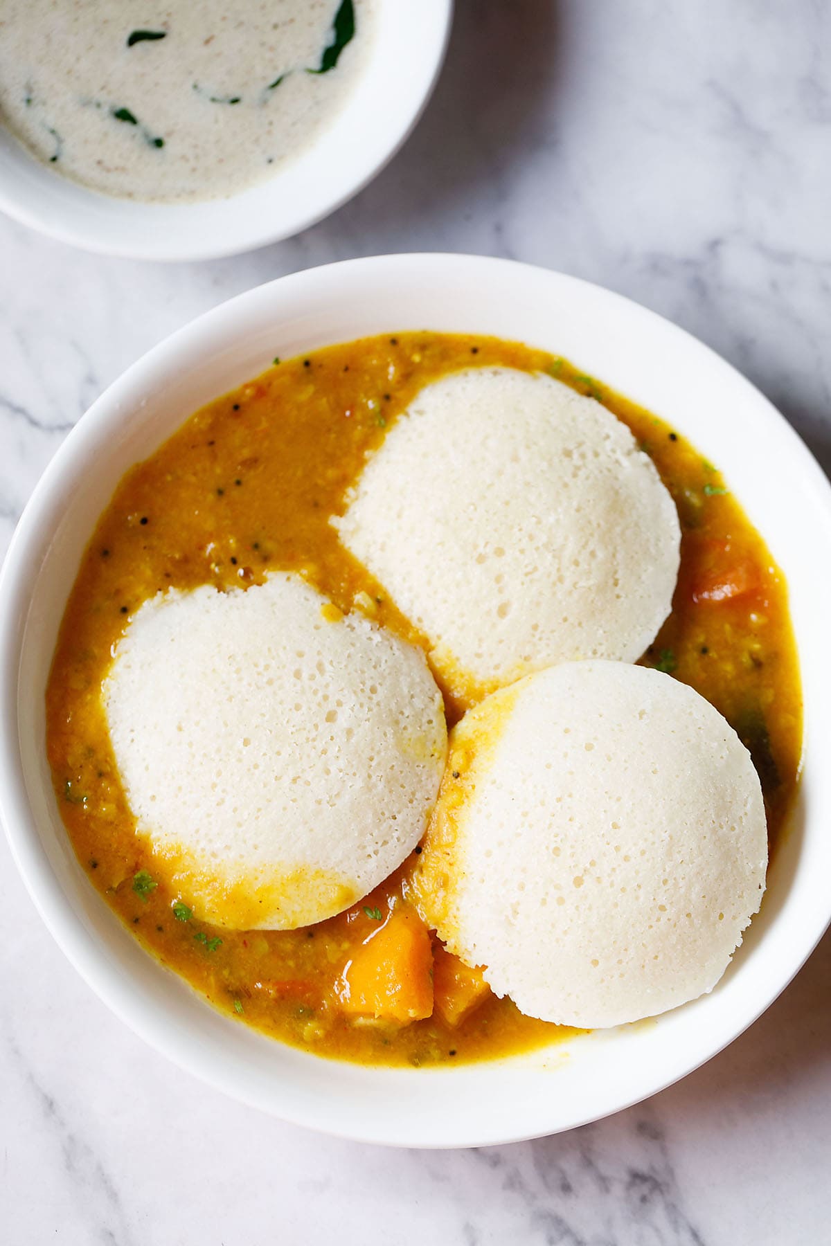 three idli on top of a layer of sambar in a white bowl
