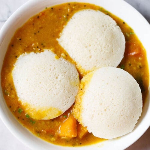 three idli on top of a layer of sambar in a white bowl