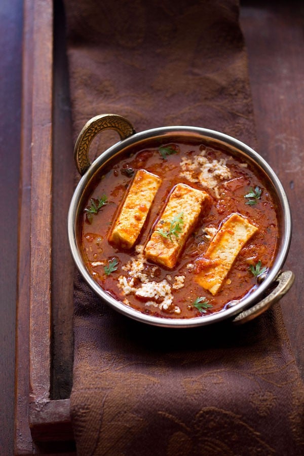 kadai paneer recipe gravy in a small copper kadai garnished with coriander sprigs and grated paneer