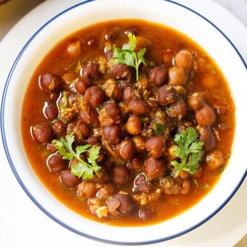 kala chana gravy with three coriander sprigs on top in a blue rimmed white bowl