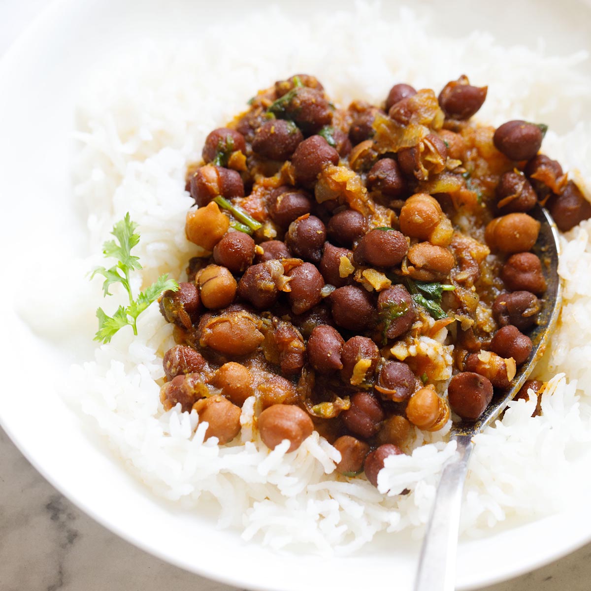 black chickpeas curry on a bed of rice with a silver spoon in a white bowl