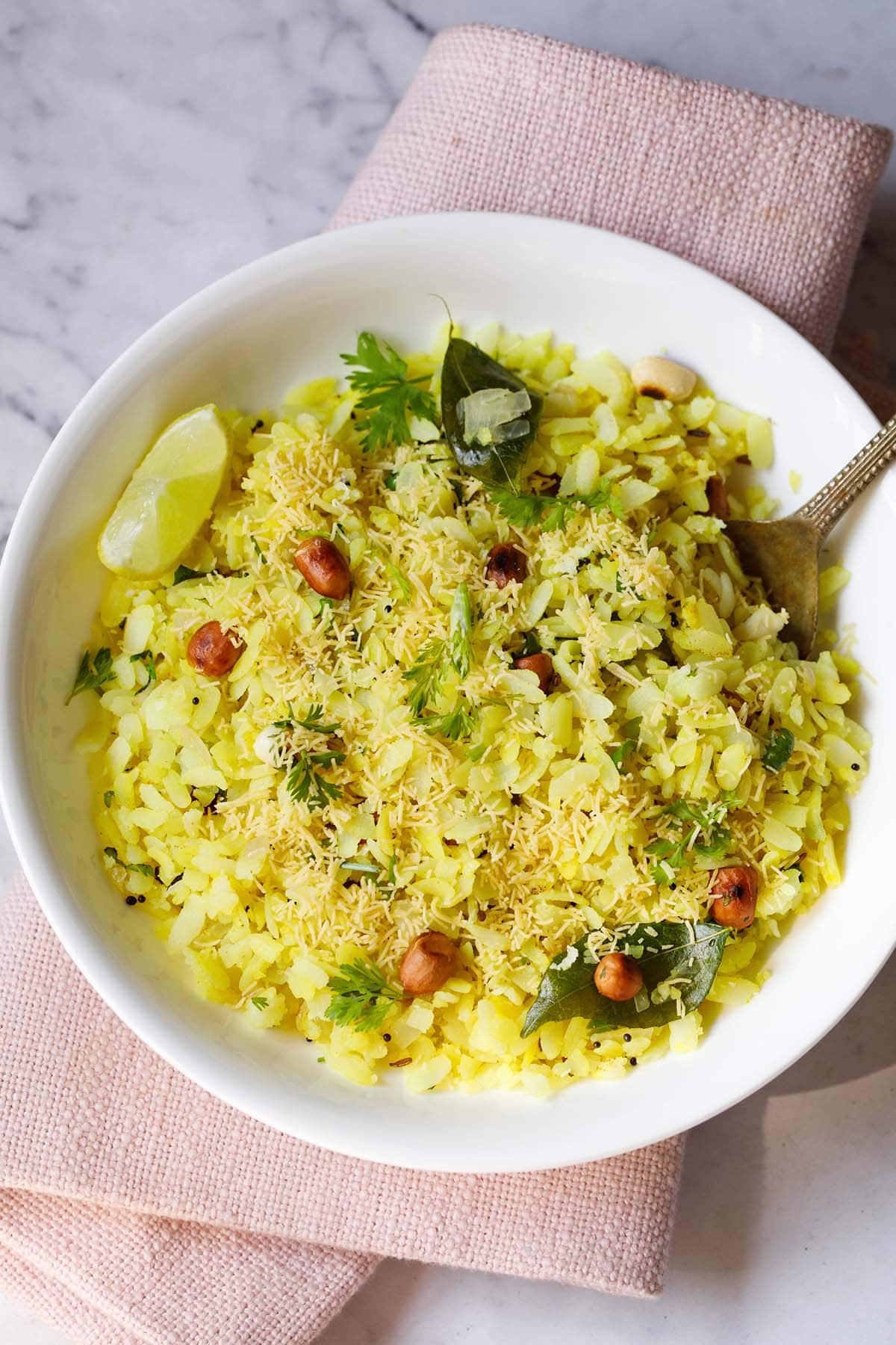 kanda poha in a white bowl with a lemon wedge and spoon.