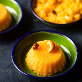 kesari with a cashew and raisin served in a dark green plate on a dark blue-black board