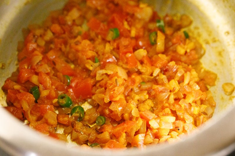 Top shot of sautéd tomatoes and khichdi ingredients in pressure cooker