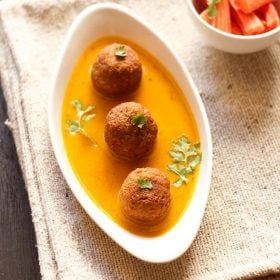 three lauki kofta in bed of curry in white oval bowl
