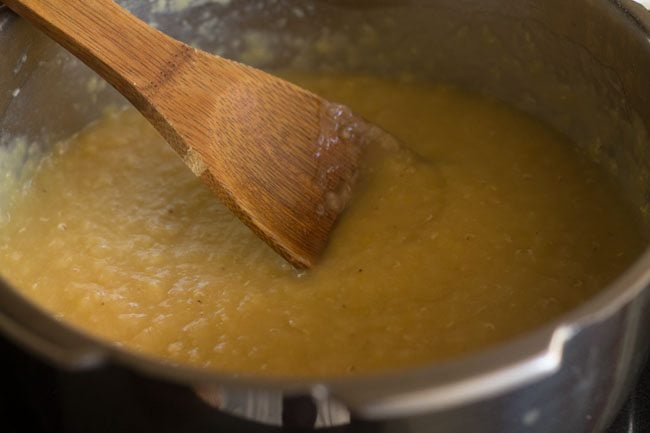 cooked masoor dal being mashed with wooden spoon.
